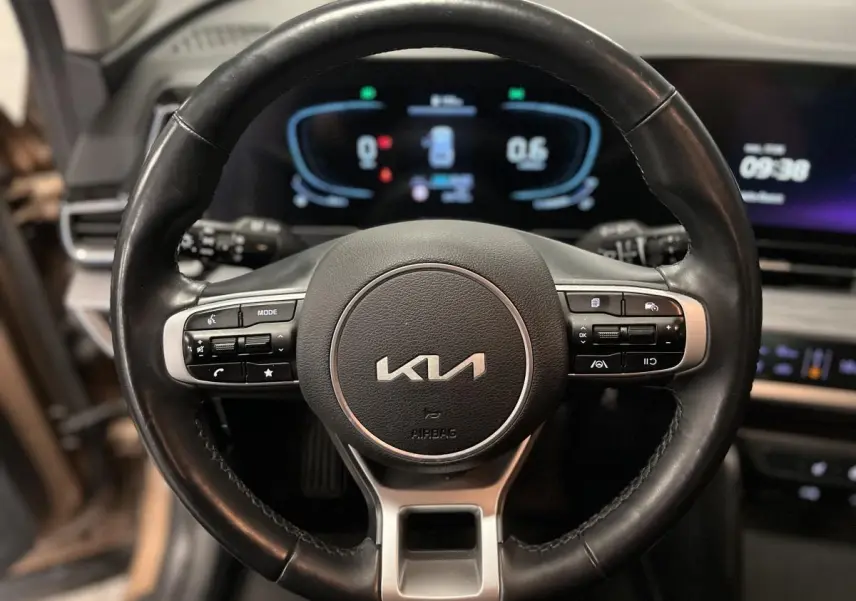 Volant cuir noir du Kia Sportage 2022 avec commandes intégrées et tableau de bord numérique lumineux en arrière-plan.