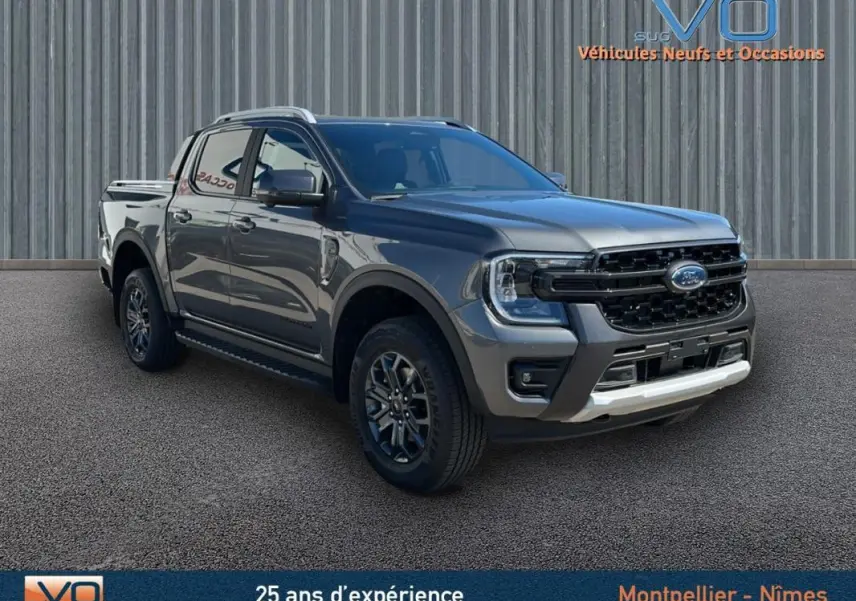 Ford Ranger gris en 3/4 avant droit, double cabine avec barres de toit et jantes alliage 17 pouces visibles.