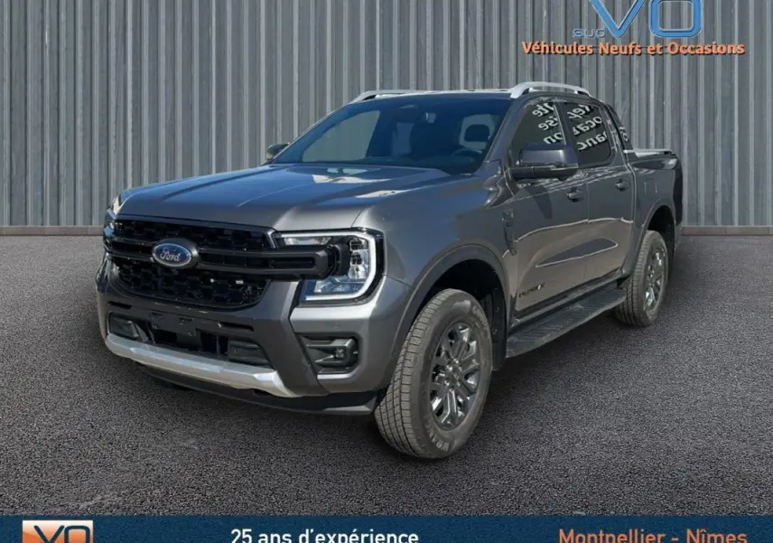 Ford Ranger Wildtrak gris en 3/4 avant droit, avec barres de toit et jantes alliage 17 pouces visibles.