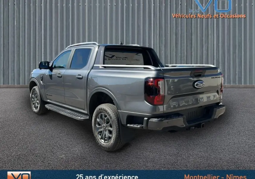 Ford Ranger Wildtrak gris en 3/4 arrière droit, avec barres de toit et vitres surteintées visibles.
