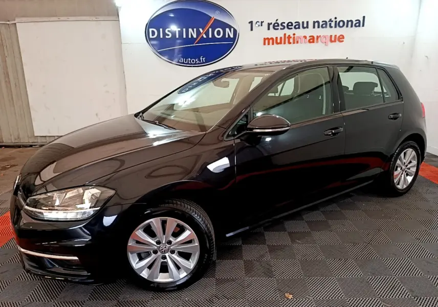 Volkswagen Golf noire vue de 3/4 avant droit, avec jantes alliage et phares halogènes visibles en intérieur showroom.