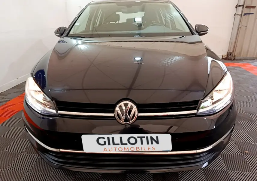 Vue frontale d'une Volkswagen Golf noire 2018 avec phares allumés et logo VW bien visible sur calandre.