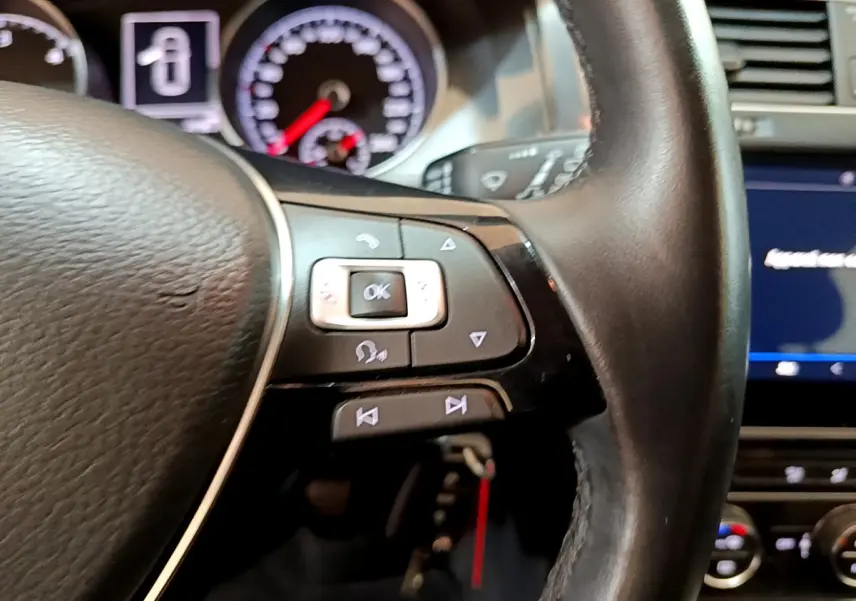 Gros plan sur le volant cuir noir de la Volkswagen Golf 2018, avec commandes multifonctions et tableau de bord en arrière-plan.