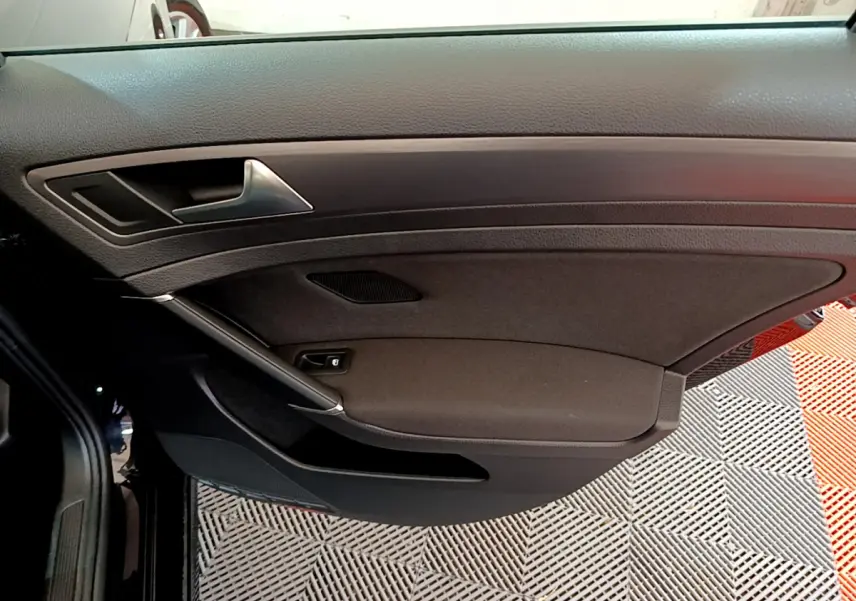 Gros plan sur la porte intérieure côté conducteur noire de la Volkswagen Golf 2018 avec poignée argentée et commande de vitre.