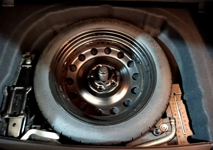 Roue de secours galette noire dans le coffre d'une Volkswagen Golf 2018, entourée des outils de changement.