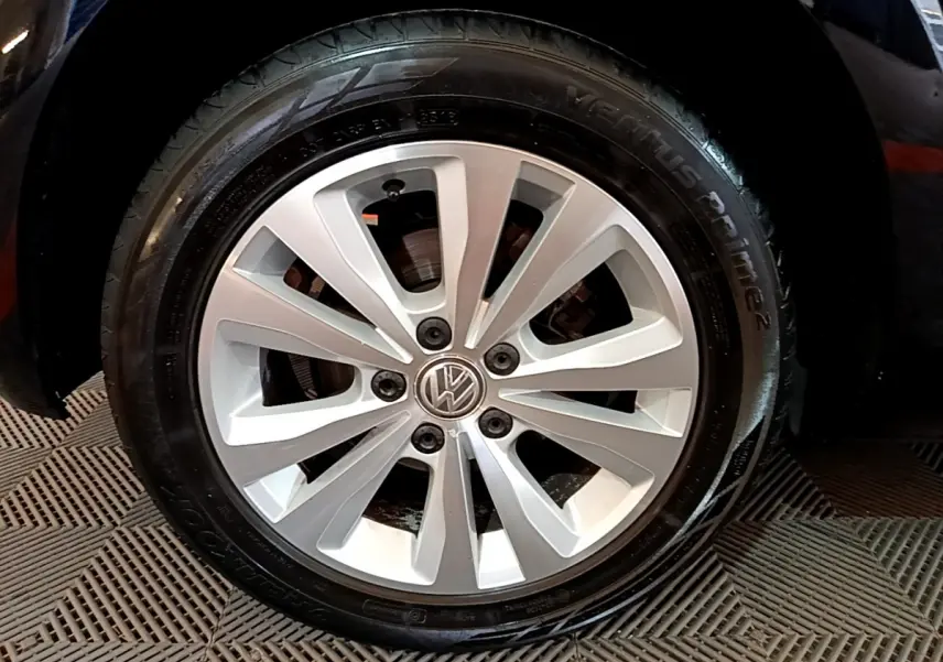 Gros plan sur la roue avant gauche d'une Volkswagen Golf noire, jante alliage argentée à 10 branches.