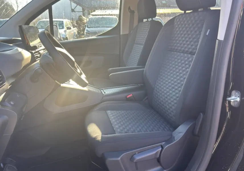 Vue intérieure côté conducteur du Peugeot Rifter noir perla nera 2025, sièges tissu gris avec accoudoir central.