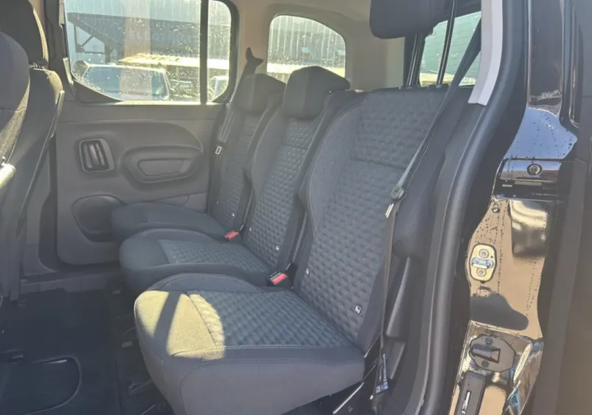 Vue latérale des sièges arrière en tissu gris foncé du Peugeot Rifter Noir Perla Nera avec porte coulissante ouverte.