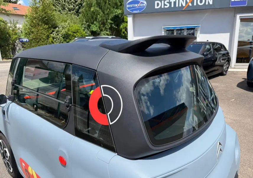 Vue 3/4 arrière droite d'une Citroën Ami MY AMI POP 2024 vert clair avec toit noir mat et logo rouge sur vitre arrière.
