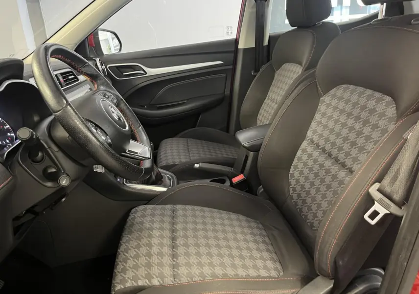 Intérieur côté conducteur du MG ZS rouge 2022 montrant sièges tissu à motif pied-de-poule et volant cuir avec surpiqûres rouges.