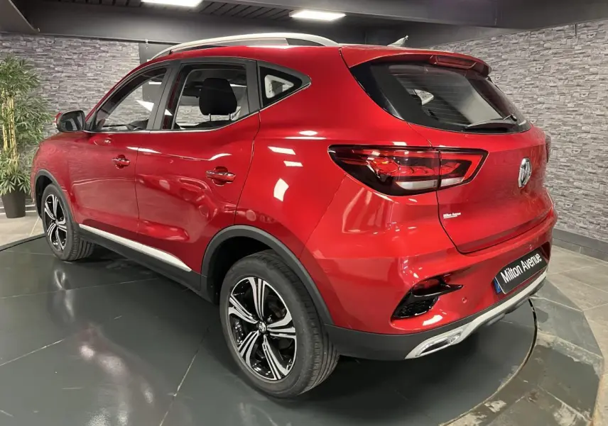 Vue 3/4 arrière droite du SUV MG ZS rouge métallisé avec jantes alliage noires et feux arrière LED dans un showroom.