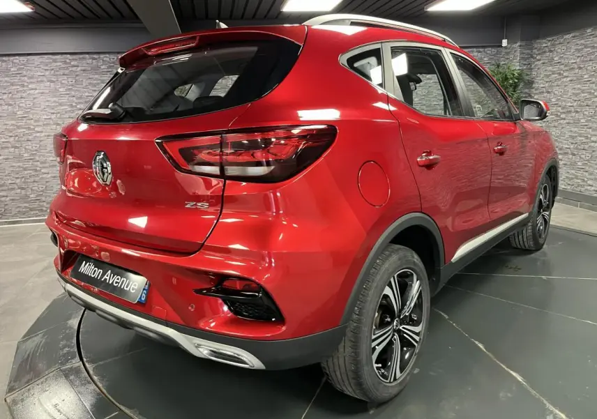 Vue 3/4 arrière droite du MG ZS rouge métallisé avec jantes alliage noires et feux arrière LED dans un showroom.