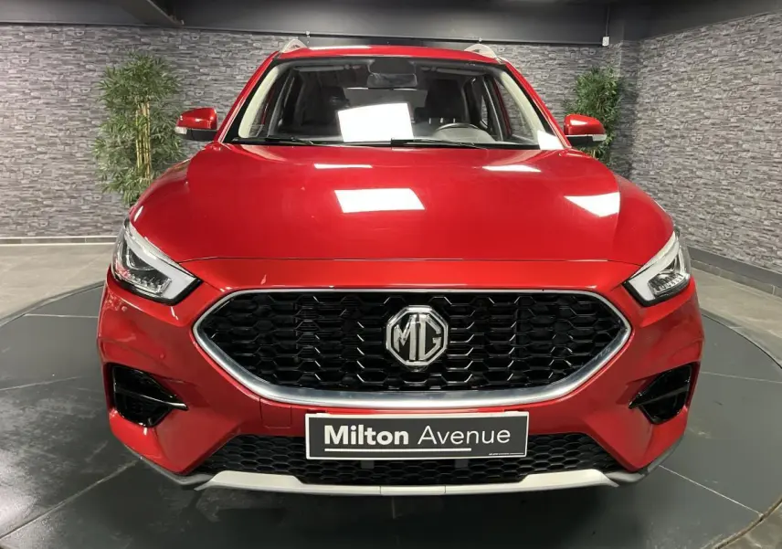 Vue frontale d'un MG ZS rouge métallisé avec calandre noire hexagonale et logo MG centré.