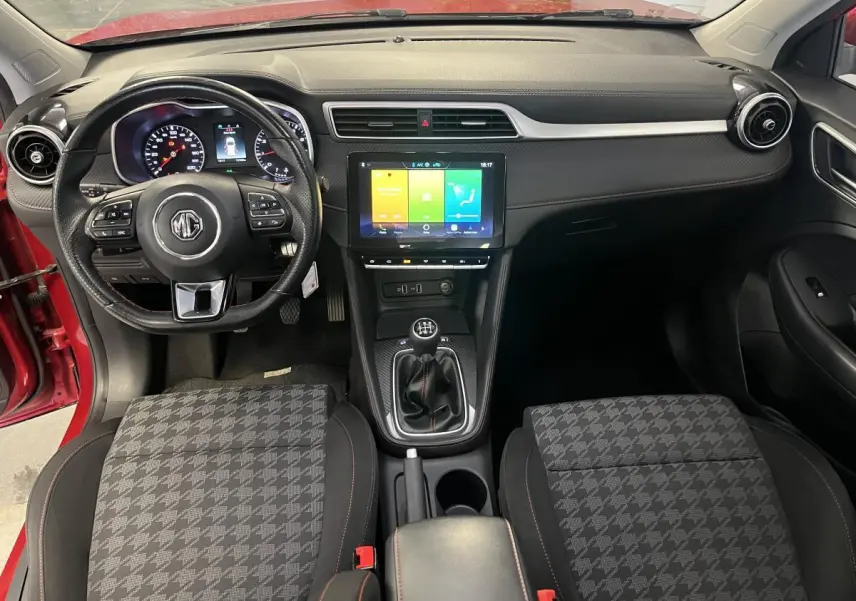 Vue intérieure avant du MG ZS rouge 2022, avec volant cuir multifonctions, écran tactile central et levier de vitesses manuel.
