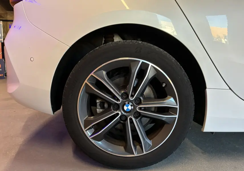 Gros plan sur la roue arrière droite d'une BMW Série 1 blanche, mettant en valeur la jante alliage bi-ton et le logo BMW central.