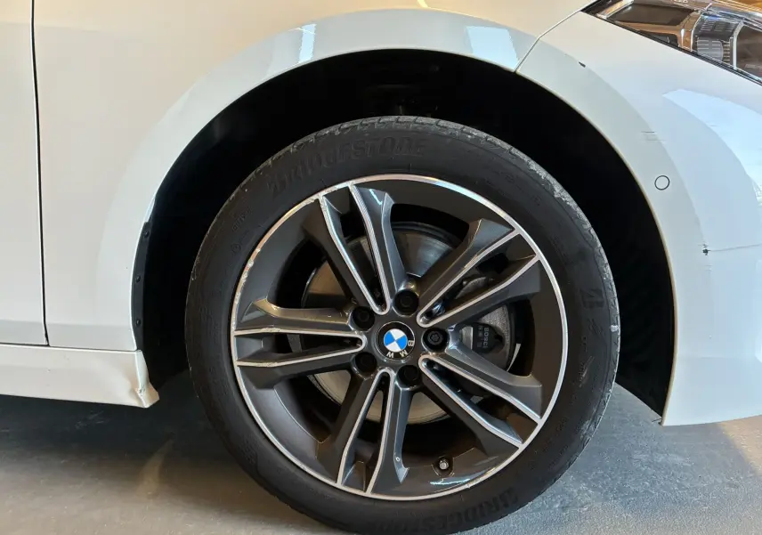 Gros plan sur la roue avant droite d’une BMW Série 1 blanche 118i Edition Sport avec jante alliage 17 pouces bicolore.
