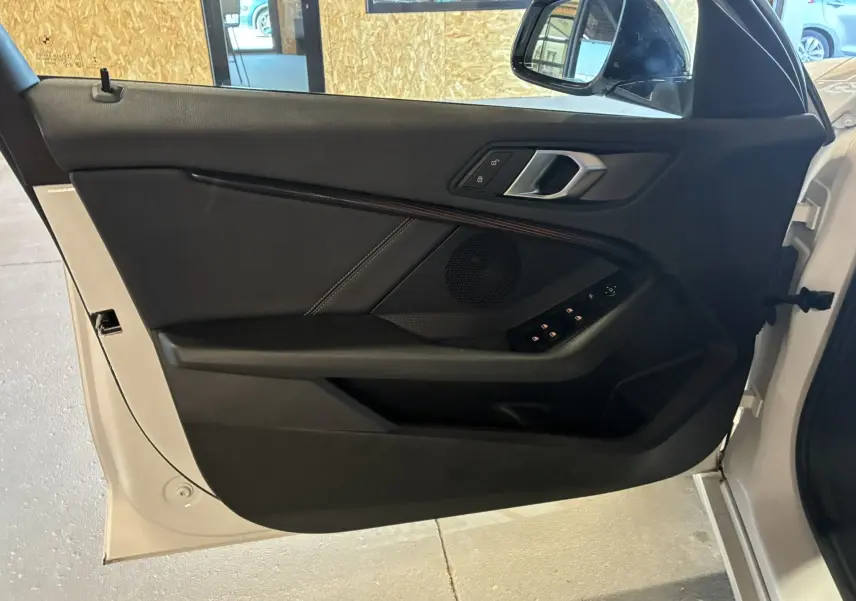 Vue intérieure de la porte avant gauche noire d'une BMW Série 1 blanche édition sport 2023 avec commandes électriques.