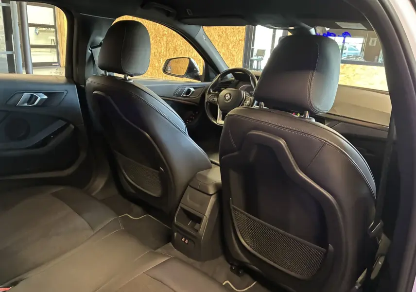 Vue intérieure arrière de la BMW Série 1 118i Edition Sport 2023 avec sièges noirs en tissu et cuir, volant visible côté gauche.