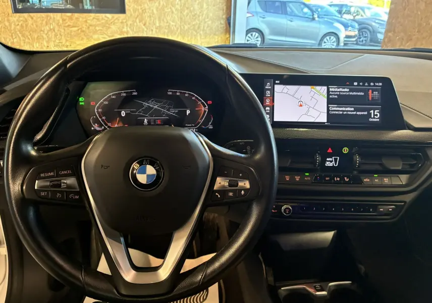 Vue intérieure de face du tableau de bord noir d'une BMW Série 1 118i Edition Sport 2023 avec écran tactile et volant multifonction.