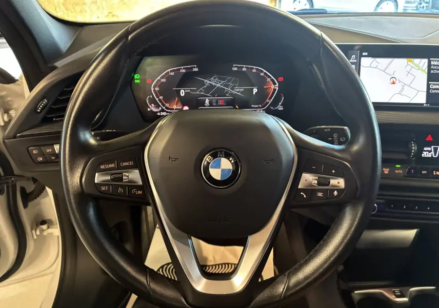 Vue rapprochée du volant en cuir noir d'une BMW Série 1 118i Edition Sport 2023 avec tableau de bord numérique et écran GPS.