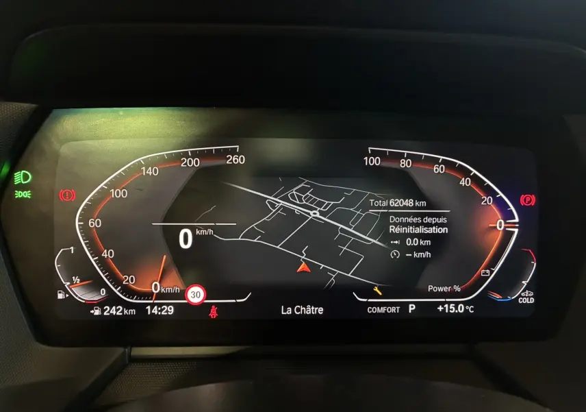 Tableau de bord numérique de BMW Série 1 blanc, affichant la vitesse à 0 km/h et la navigation GPS active.