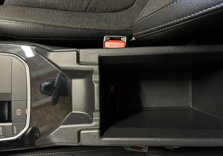 Vue plongeante sur la console centrale noire avec rangement ouvert et sièges en tissu noir dans une BMW Série 1 blanche.