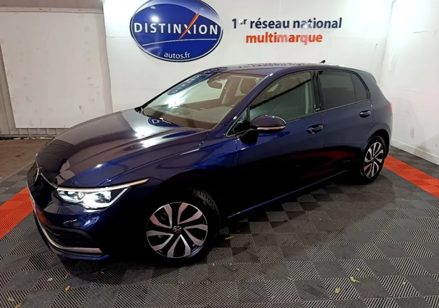 Volkswagen Golf 1.0 TSI bleu en 3/4 avant droit avec phares allumés dans un showroom intérieur.