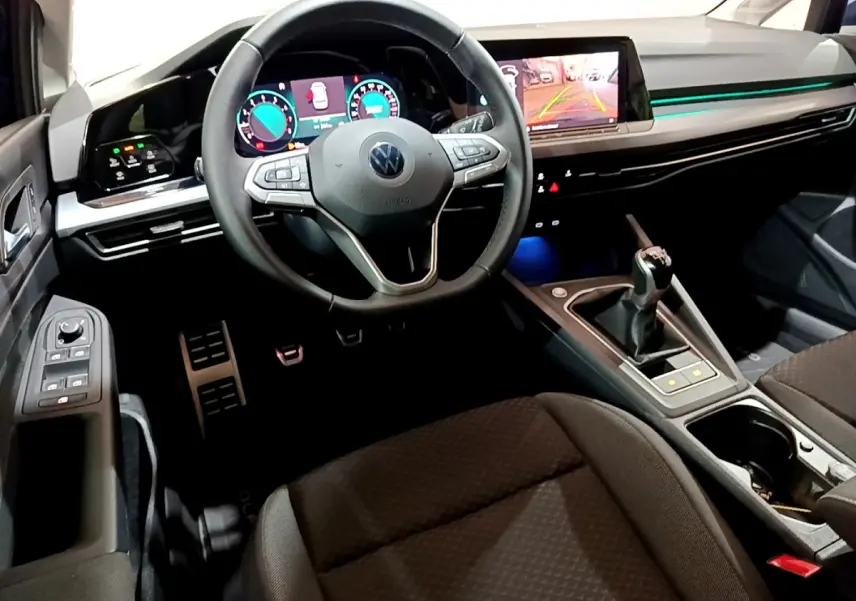 Vue intérieure avant de la Volkswagen Golf 1.0 TSI avec volant cuir, écran tactile et levier de vitesse manuel.