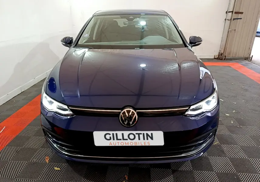 Vue frontale d'une Volkswagen Golf 1.0 TSI bleu nuit avec phares LED allumés dans un garage.