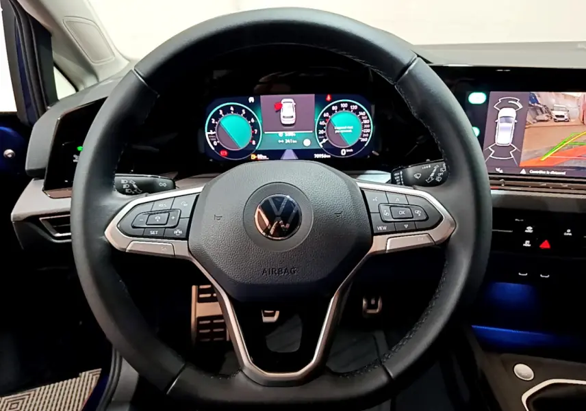 Vue centrée sur le volant cuir multifonctions et les écrans digitaux du tableau de bord de la Volkswagen Golf bleue 2022.