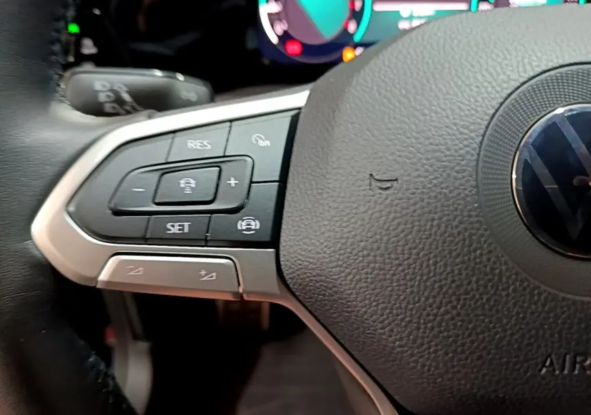 Gros plan sur le volant cuir multifonctions de la Volkswagen Golf 1.0 TSI bleu, avec commandes de régulateur de vitesse visibles.