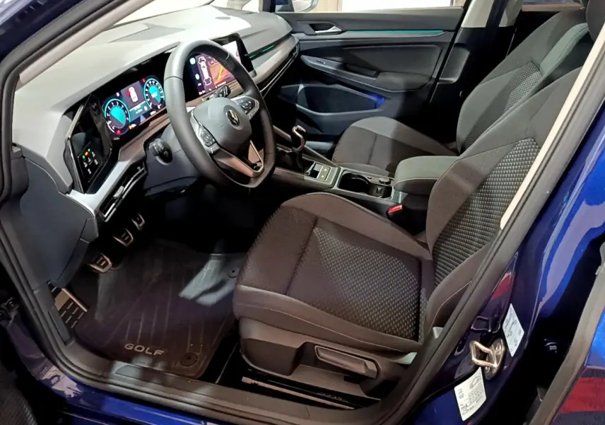 Vue intérieure côté conducteur d'une Volkswagen Golf bleue 2022 avec tableau de bord numérique et sièges tissu noirs.