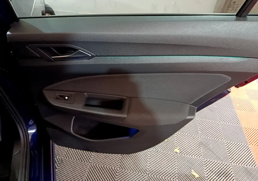 Porte côté gauche ouverte d'une Volkswagen Golf 1.0 TSI bleu 2022, avec poignée intérieure et commande de lève-vitre.