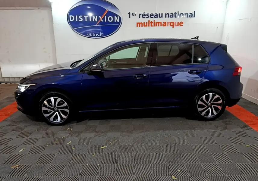 Profil latéral droit d'une Volkswagen Golf 1.0 TSI bleu foncé dans un showroom avec logo Distinxion en arrière-plan.