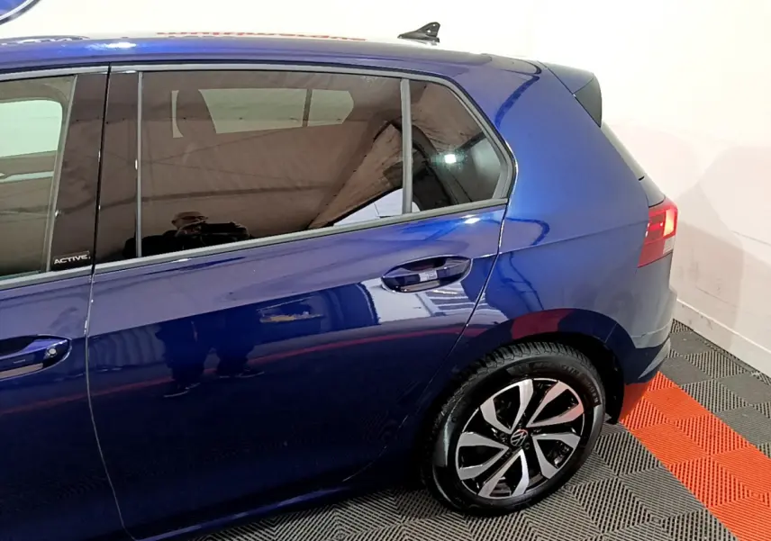 Vue côté gauche arrière d'une Volkswagen Golf 1.0 TSI Active bleu avec jante alliage et vitres teintées.