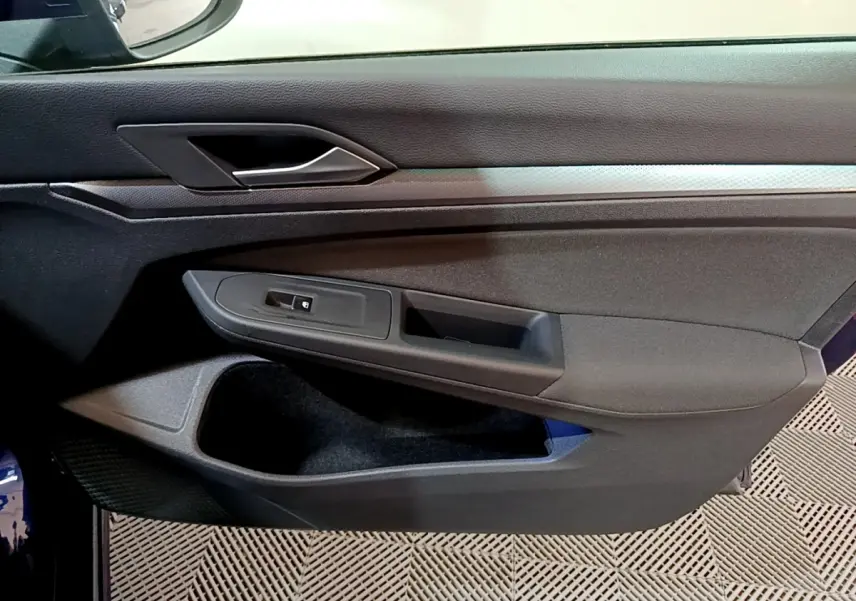 Vue rapprochée de la porte côté gauche d'une Volkswagen Golf bleu 2022 avec poignée argentée et commandes de vitre noires.