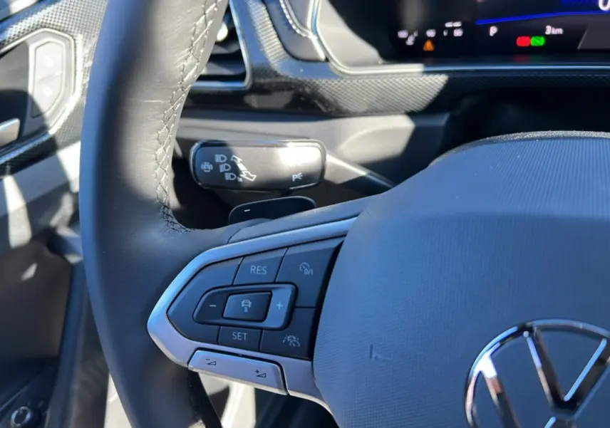 Gros plan sur le volant cuir multifonctions côté gauche du Volkswagen T-Cross blanc avec commandes de régulateur adaptatif.