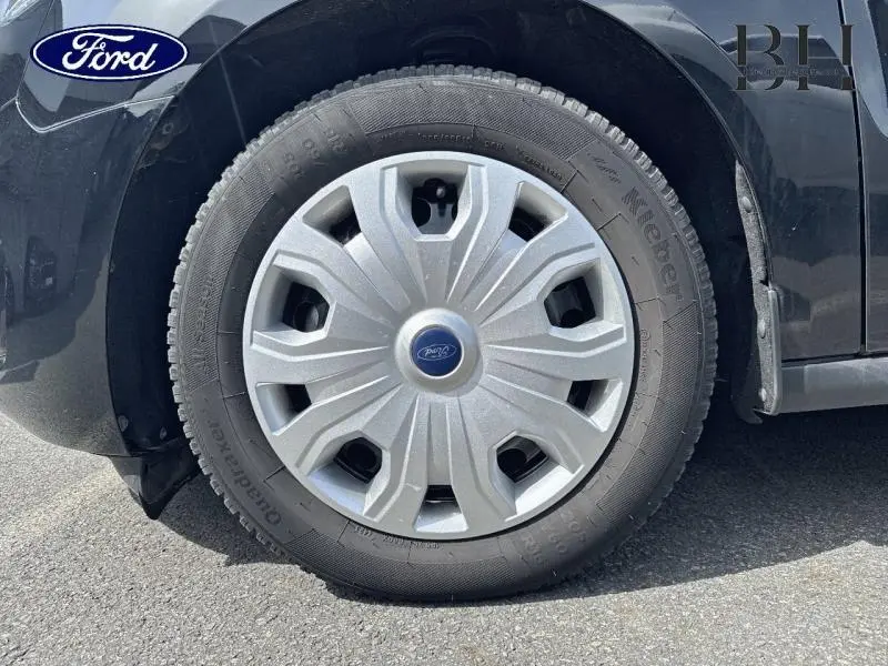 Gros plan sur la roue avant gauche du Ford Transit Connect noir Agate Métallisée avec enjoliveur gris et logo Ford central.