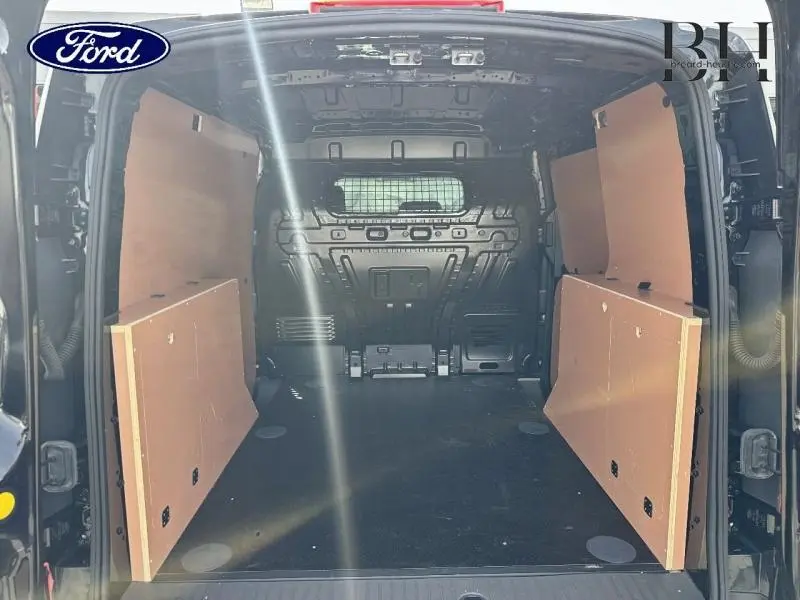 Vue arrière intérieure du Ford Transit Connect noir Agate Métallisée, montrant l’espace de chargement avec cloison vitrée et panneaux latéraux en bois.
