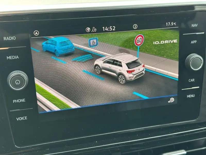 Affichage numérique montrant une Volkswagen T-Roc grise vue de trois quarts arrière droite sur une route avec signalisation 60 km/h