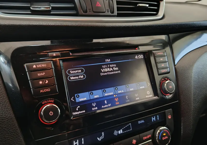 Gros plan sur l’écran tactile et la console centrale noire du Nissan Qashqai gris clair, affichant la radio FM et la climatisation.
