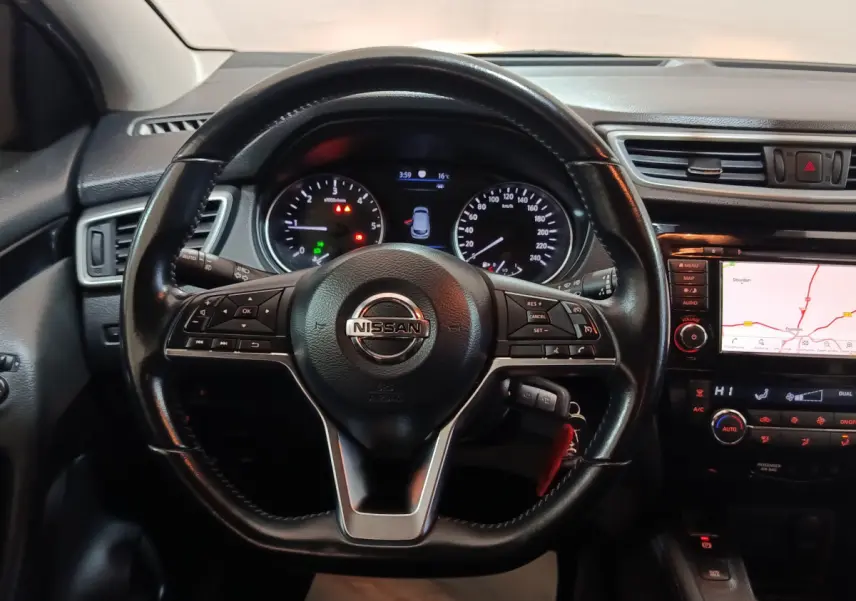Vue intérieure centrée sur le volant cuir du Nissan Qashqai 2019 avec tableau de bord et écran tactile de navigation allumé.