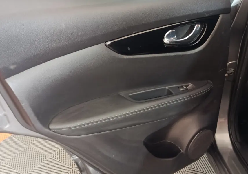 Vue rapprochée de la porte intérieure côté gauche du Nissan Qashqai gris clair, avec poignée chrome et commande de vitre.