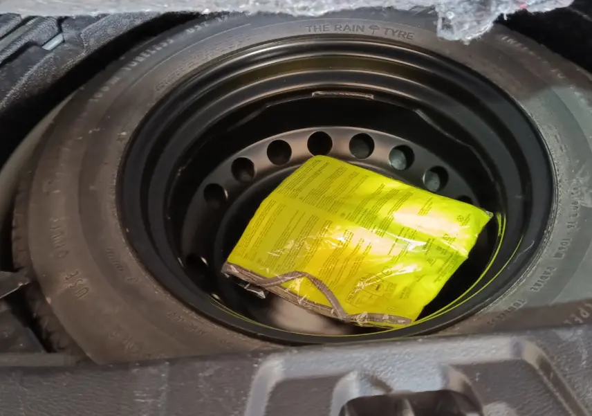 Gros plan sur la roue de secours galette noire avec un emballage jaune visible dans le coffre du Nissan Qashqai gris clair.