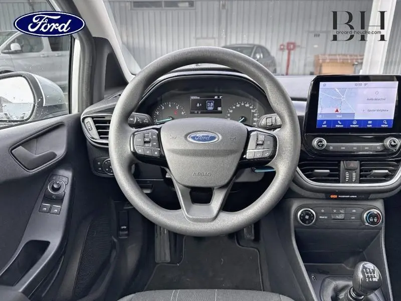 Vue intérieure centrée sur le volant et tableau de bord de la Ford Fiesta gris lunaire avec écran tactile et boîte manuelle.