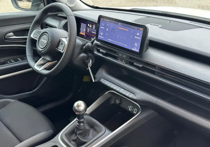 Vue intérieure côté conducteur du Jeep Avenger 2024, tableau de bord noir avec écran tactile et levier de vitesse manuel.