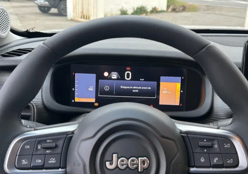Vue intérieure centrée sur le volant Jeep noir avec tableau de bord numérique affichant 0 km/h et alertes.