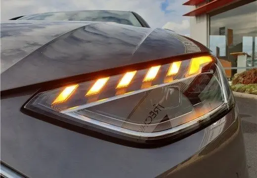 Gros plan sur le phare avant droit allumé de l'Audi A4 Avant Business 30 TDI gris Terra de 2020.