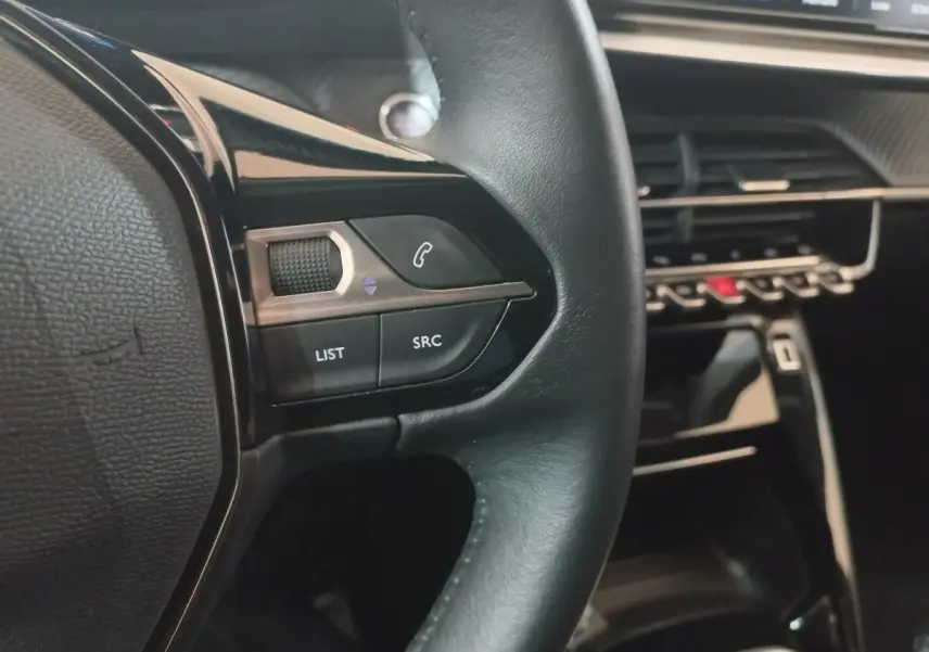 Gros plan sur le volant cuir noir de la Peugeot 2008 2021 avec commandes audio et tableau de bord moderne.