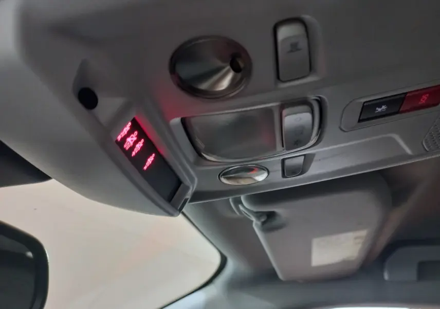Vue intérieure du plafond avant de la Peugeot 2008 orange, montrant les commandes d'éclairage et le panneau SOS lumineux rouge.